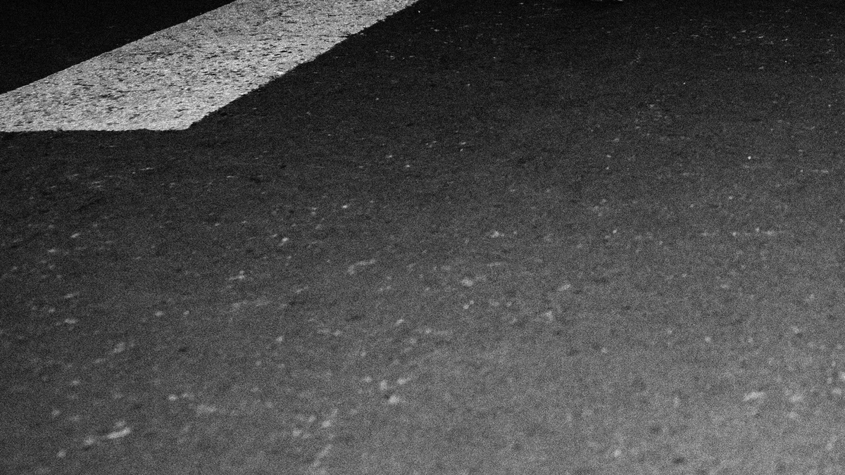 Black and white close-up of dark asphalt or concrete with a white painted edge in the upper left corner.